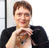 Smiling woman, holding glasses, looking at the camera.